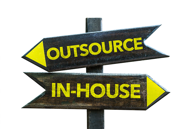 An image showing two signs pointing in opposite directions. One sign reads outsource the other in-house.